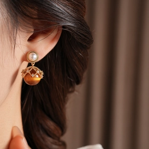 Close-up of vintage golden tiger eye earrings with white pearl detail on model