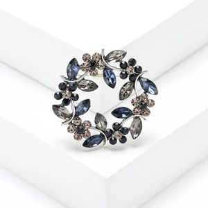 Elegant silver-tone wreath brooch with navy and dark grey crystals on white pedestal
