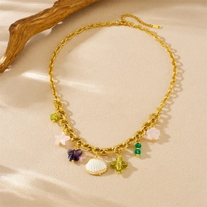 Collier en acier doré avec pendentifs trèfle, coquillage, fleur et papillon sur le sable