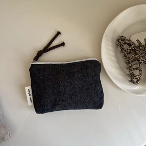 Detail view of mini denim canvas pouch with white zipper and brown braided puller