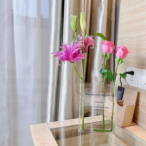 Detailed view of a clear acrylic book vase with pink lilies on a wooden table