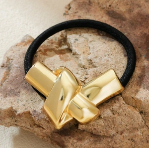 Detailed macro view of a gold minimalist metal knot hair tie on a natural rock background