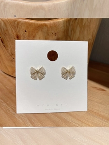 Detail of bow-shaped stud earrings with white faux pearls and gold-plated base