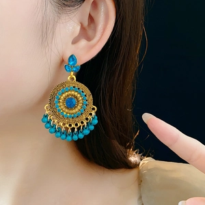 Dettaglio di orecchini vintage dorati con strass blu e nappine pendenti in perline