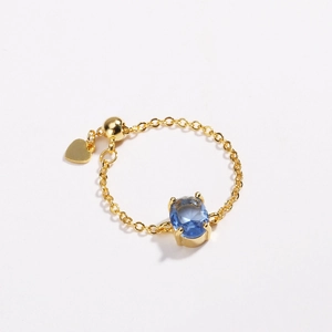 Macro detail of adjustable gold plated ring with blue oval zircon and heart charm