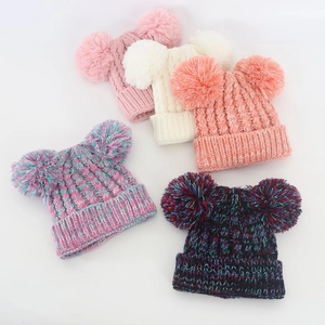 Flat lay of colorful knitted baby beanies with double pom-poms showing knit textures