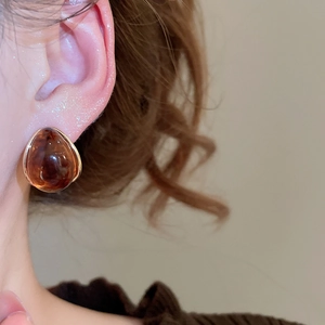 Close-up of amber resin teardrop earring with gold metal trim worn by a model