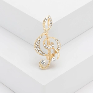 Elegant gold musical note brooch with sparkling crystals on white geometric stand