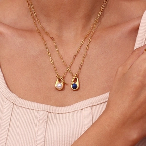 Detail of layered 18K gold-plated necklaces with pearl and blue sapphire pendants on a model