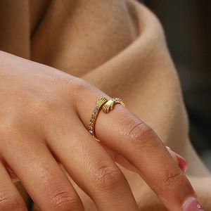 Detail of gold hugging hands ring with zircon inlays on fingers of a female model