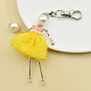 Detail of handmade ballerina keychain with yellow tutu and pearl head on ceramic plate
