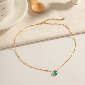 Detail of a gold-tone necklace featuring a blue heart-shaped opal pendant on a soft fabric background