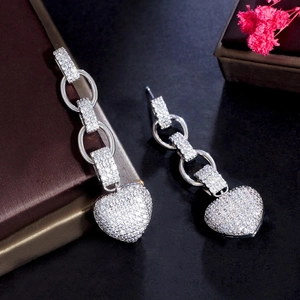 Detailed view of silver heart drop earrings featuring micro-pave crystals on dark leather
