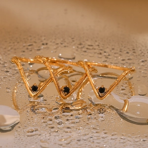 Macro shot of three gold V-shaped rings with black stones on a wet surface