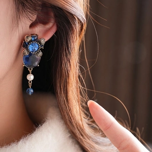 Vintage gold-plated floral earrings with deep blue oval gemstones worn by a model
