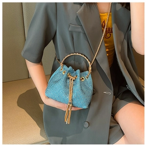 Close-up of blue rhinestone bucket bag with golden circular handle and chain strap on model