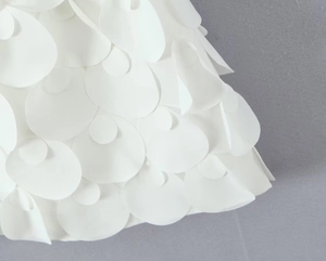 Dettaglio macro di un abito bianco con texture a squame 3D e petali stratificati