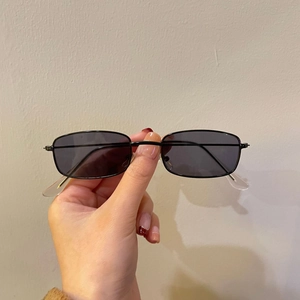 Detail view of vintage black oval metal frame sunglasses held by hand in soft light