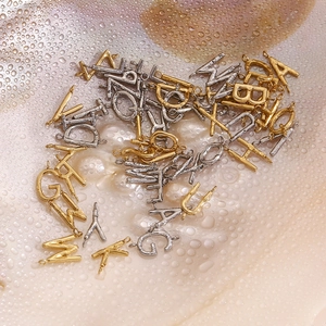 Golden and silver metal letter charms scattered on a textured shell surface with water drops