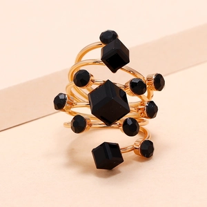 Golden spiral ring featuring black geometric cubes and round stones on a warm background