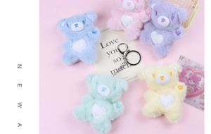 Five colorful plush bears with heart patches and metal keychains displayed on pink background
