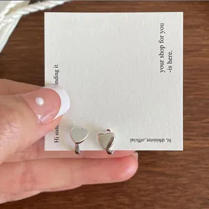 Close-up of polished silver heart earrings on a white display card with metal buckle design
