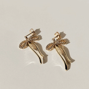 Elegante goldene Schleifenohrringe mit Mikro-Steinen und langen Quasten auf beigem Grund