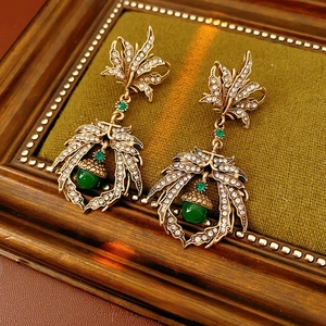 Vintage gold leaf earrings with green emerald gems and crystals on a velvet display