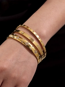 Close-up of three gold stainless steel bangles set with zircon stars and flowers