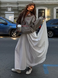 Street style view of a long white pleated maxi skirt paired with a grey track jacket