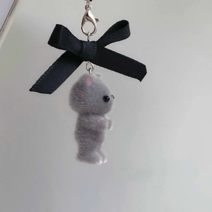 Detail of grey flocked kitten plush charm with oversized black bow and metal clasp