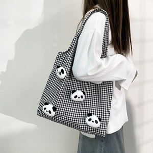 Detail of checkered canvas tote bag with 3D panda dolls on a model shoulder