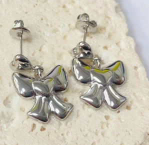 Detailed view of polished silver bow stud earrings with heart center on stone background