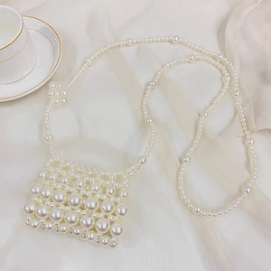 Detail of handmade mini pearl woven crossbody bag on elegant cream silk fabric background