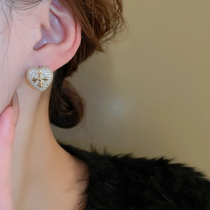 Close-up of heart cross stud earring with white zircon inlay on model's ear