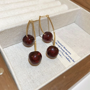 Macro view of dark red resin cherry earrings with gold hooks in a jewelry box