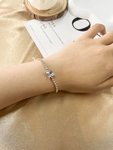 Close-up of golden tennis bracelet with square-cut clear stone on elegant silk fabric