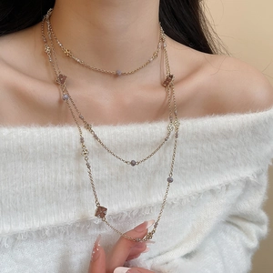 Detail of layered gold necklaces with clover pendants on a white knitted sweater