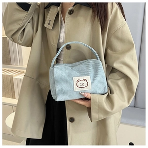 Detail of light blue corduroy handbag featuring a minimalist brown bear patch detail