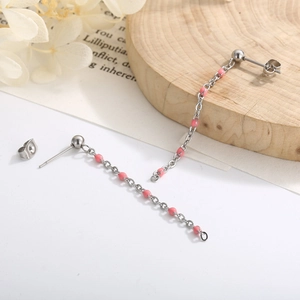 Detail of silver chain tassel earrings with pink beads on a rustic wooden backdrop