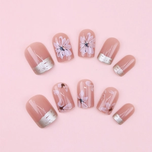 Detail of handmade press-on nails featuring white floral patterns and silver foil accents