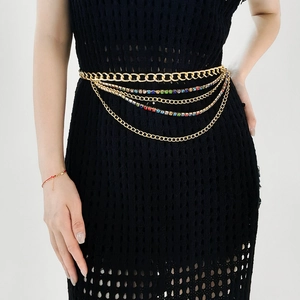 Détail d'une chaîne de taille dorée multicouche avec strass colorés sur robe