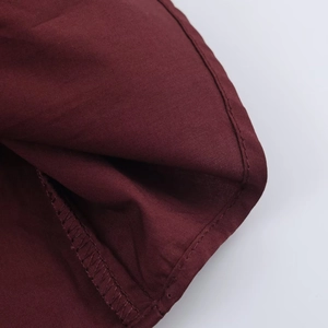 Detail of burgundy poplin fabric showing double-stitched edges and fine woven texture