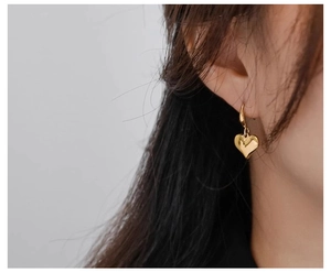 Detail of a shiny gold 3D heart pendant earring worn to show the drop length and polish