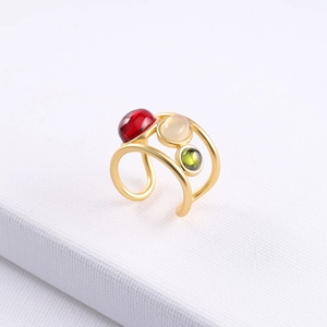 Detail of adjustable gold ring featuring round red, white, and green gemstones on white background