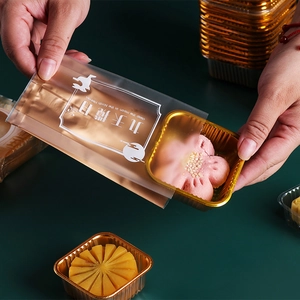 Close-up of hand placing a pink flower mooncake into a golden PET plastic tray and bag