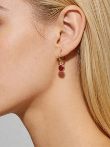 Close-up of a gold hoop earring with a round red ruby pendant worn by a model