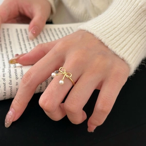 Detail of a golden bow ring with white pearls worn by a model holding a classic book