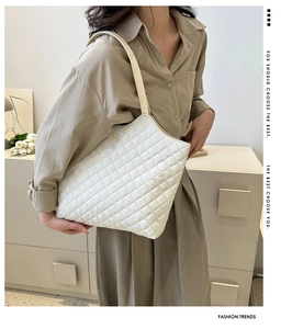 Détail du sac cabas matelassé blanc avec un logo trèfle en métal sur le côté du sac