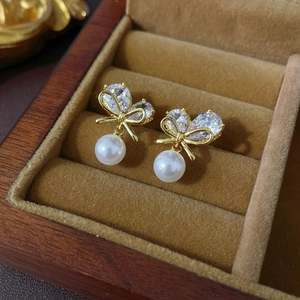 Detail of bow-shaped zircon earrings with white pearl drop in a luxury wooden box